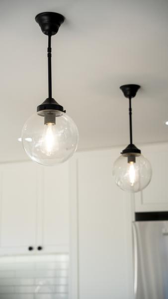 Two modern black pendant lights with clear glass globes hanging over white kitchen cabinetry