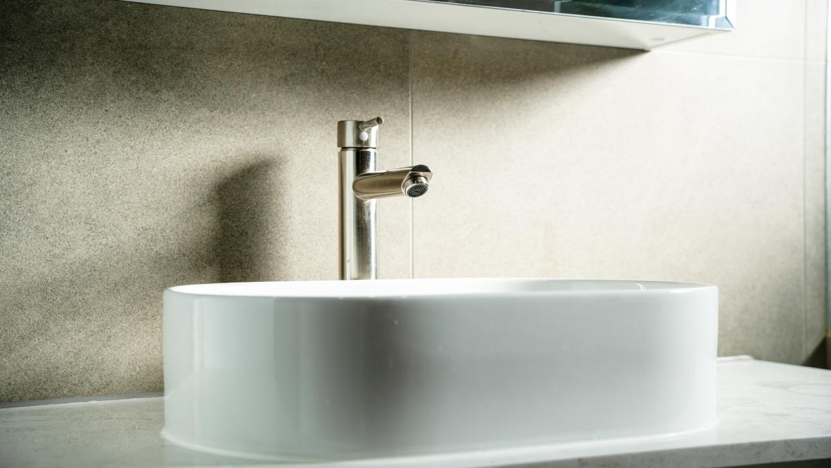 Modern white ceramic basin with chrome tap against speckled stone benchtop in luxury bathroom renovation