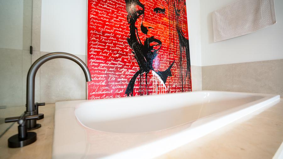 Modern luxury bathroom with white marble bathtub, black tapware and vibrant red pop art on white tiled wall
