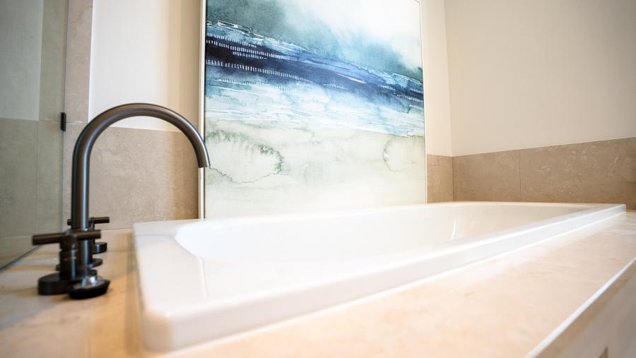 Luxury bathroom renovation featuring modern black tapware, white bathtub and ocean-themed artwork