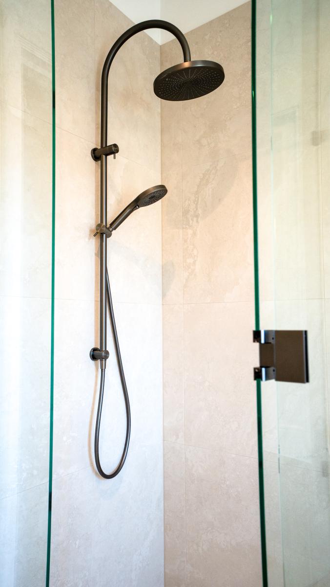 Luxury bathroom shower featuring black rainfall showerhead and handheld unit on marble-effect wall tiles