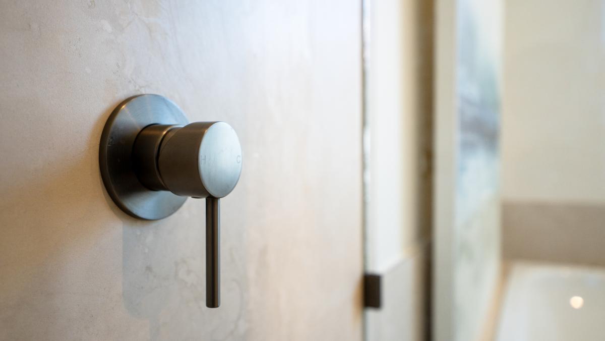 Modern brushed brass bathroom tap mixer with circular wall plate and lever handle on marble wall