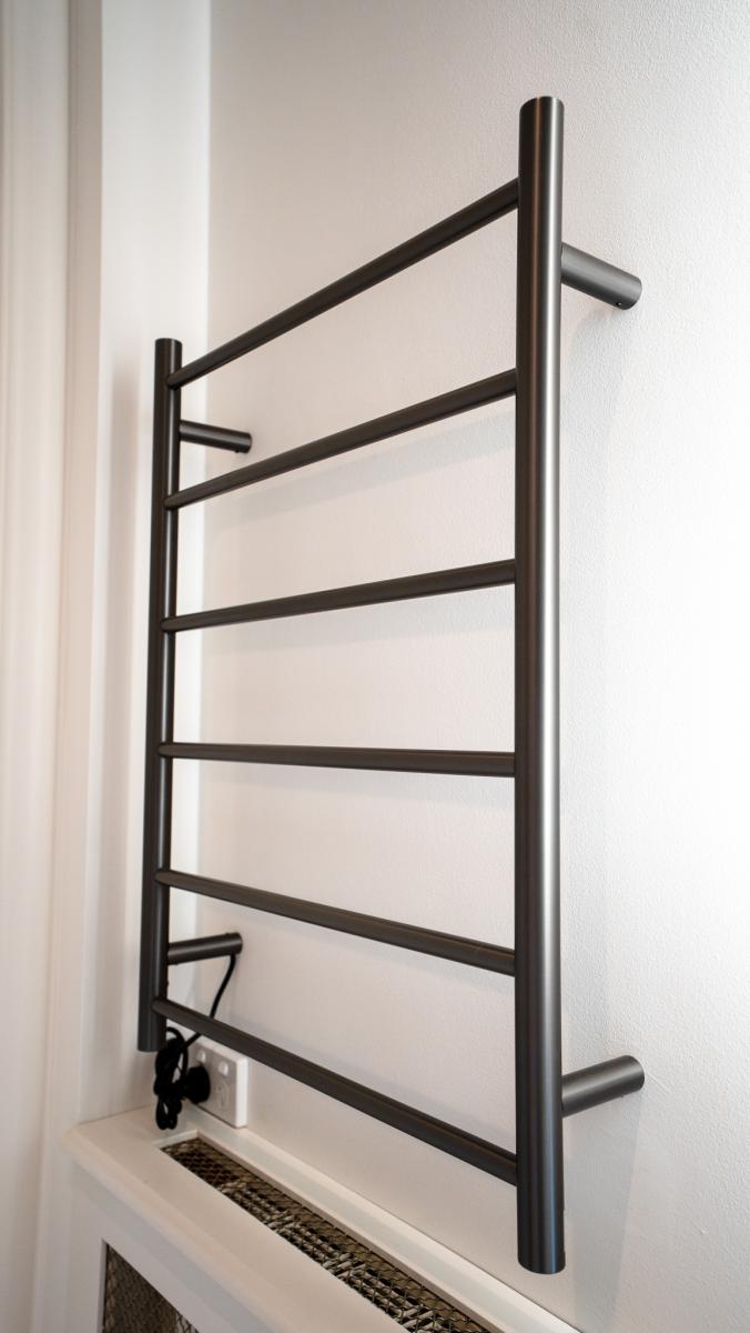 Modern black heated towel rail mounted on white bathroom wall with electrical connection