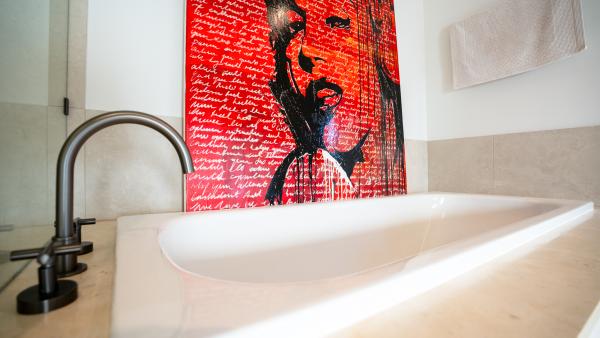 Luxury freestanding bathtub with black tap and vibrant red pop art portrait on bathroom wall
