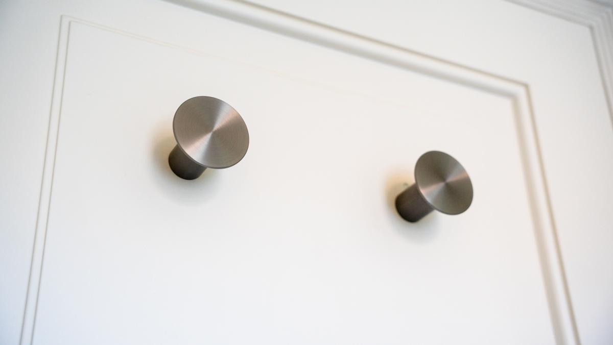 Two brushed stainless steel cabinet knobs mounted on white shaker-style kitchen cabinet door with raised panel detail