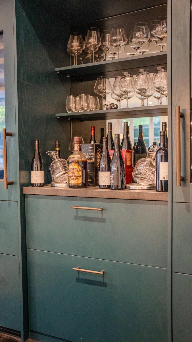 Elegant sage green kitchen bar area with premium wine storage, crystal glassware and brass handles