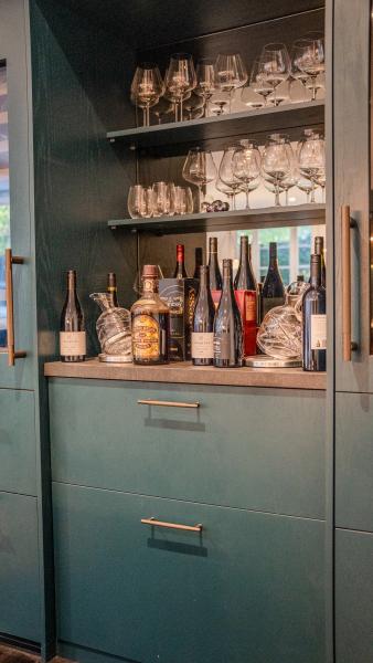 Elegant sage green kitchen bar area with premium wine storage, crystal glassware and brass handles