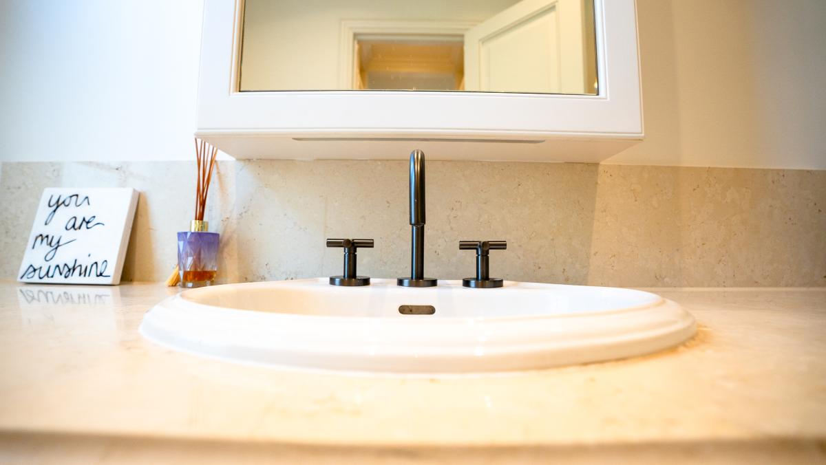 Luxury bathroom sink with white basin, black taps, and stone benchtop featuring decorative accessories