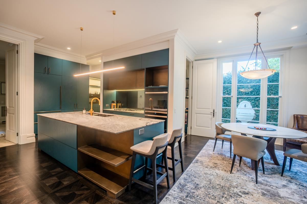 Modern luxury kitchen with teal cabinets, marble island, and open dining area with pendant lighting