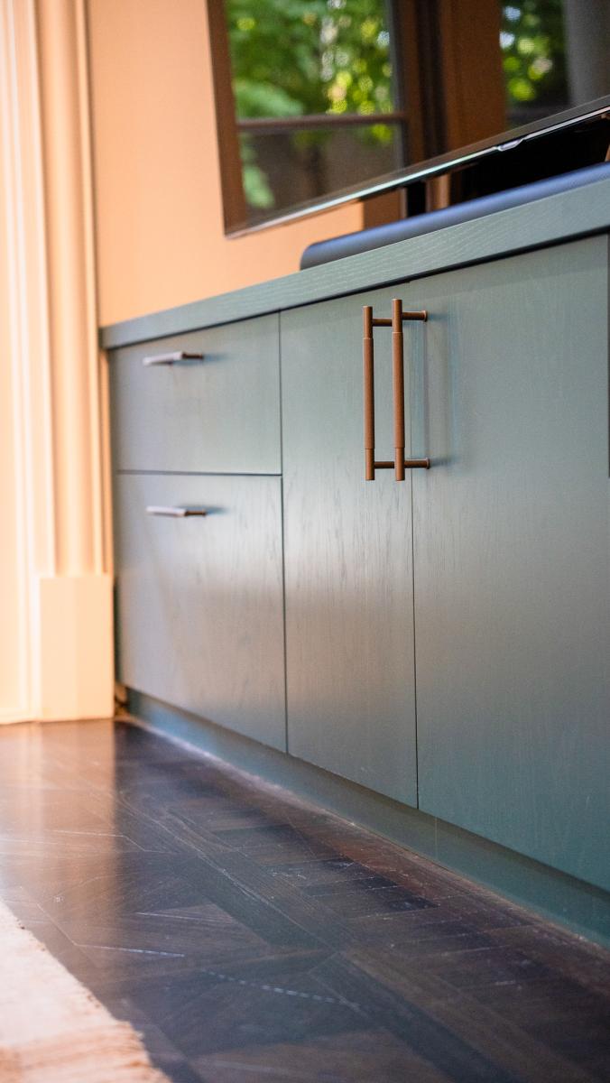 Modern sage green kitchen cabinetry with brass handles and dark timber flooring