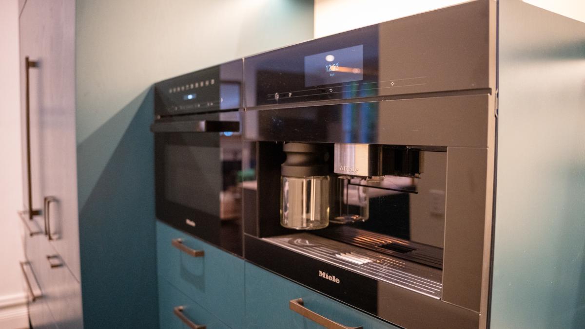 Built-in Miele coffee machine and oven in modern teal kitchen with stainless steel finishes