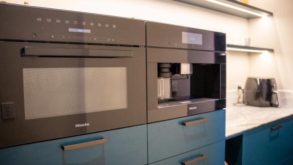 Luxury kitchen featuring built-in Miele appliances with blue cabinets and brass handles on white stone benchtops