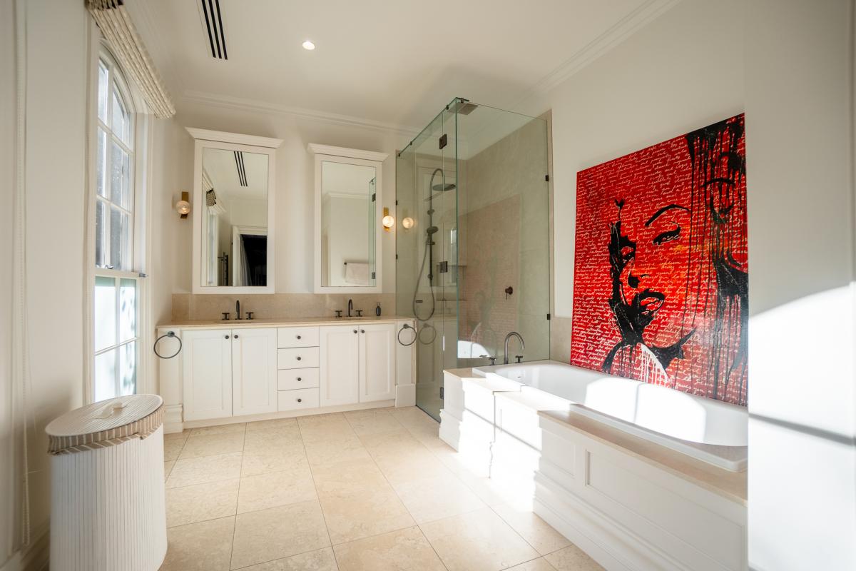 Luxury bathroom renovation with white vanity, glass shower, soaking tub and contemporary red artwork