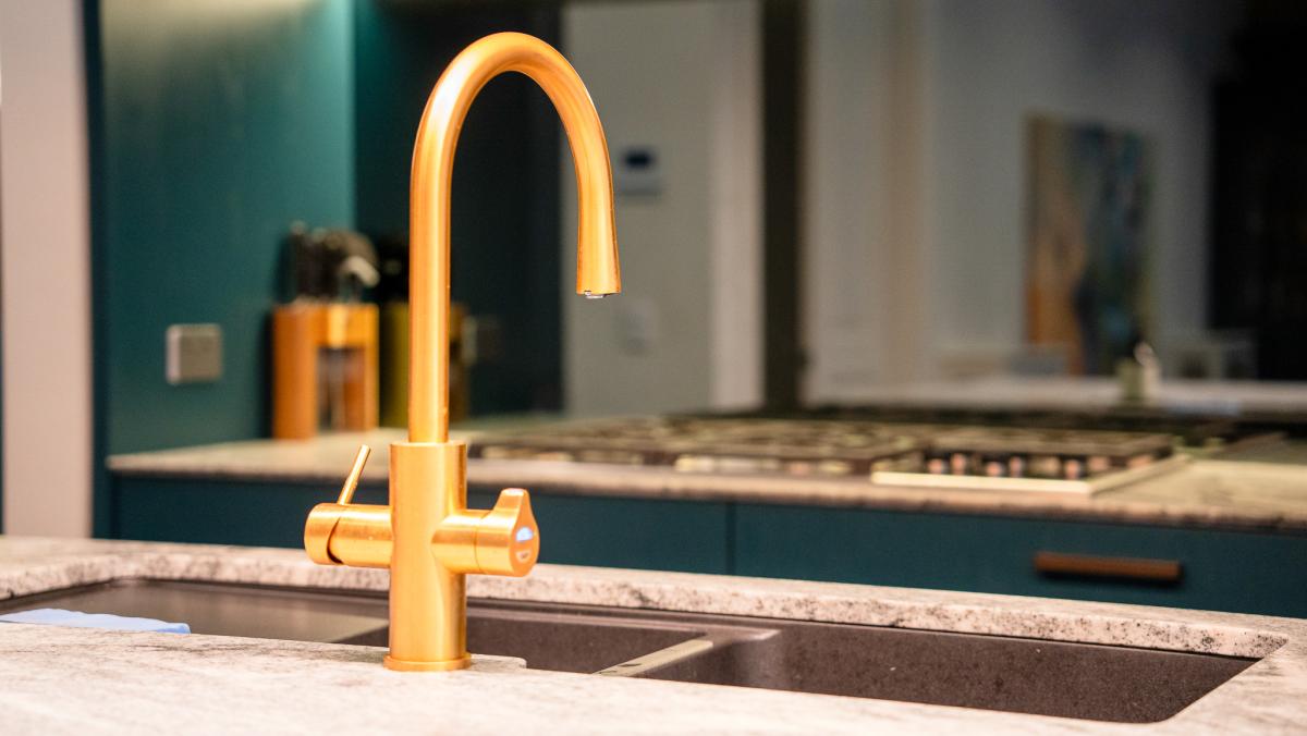 Luxury gold kitchen tap on speckled granite worktop in modern teal kitchen renovation