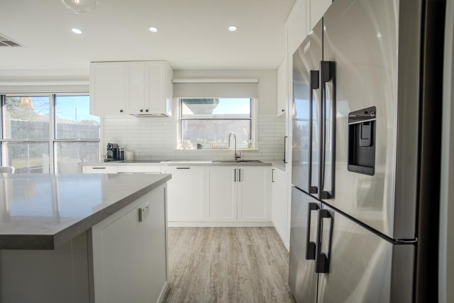 Modern white kitchen with island, stainless steel appliances, grey stone benchtops and subway tile splashback