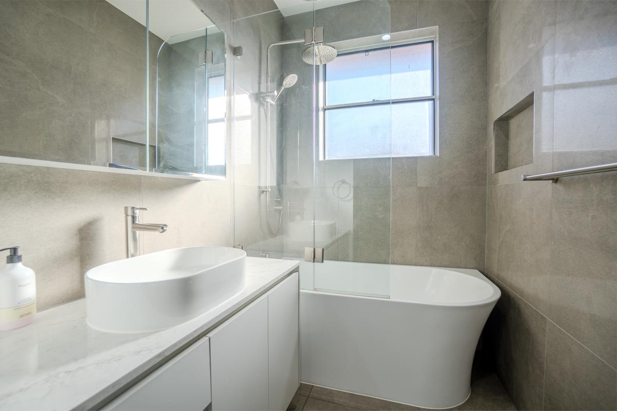 Modern luxury bathroom with freestanding bathtub, glass shower screen, white vanity and grey stone tiles