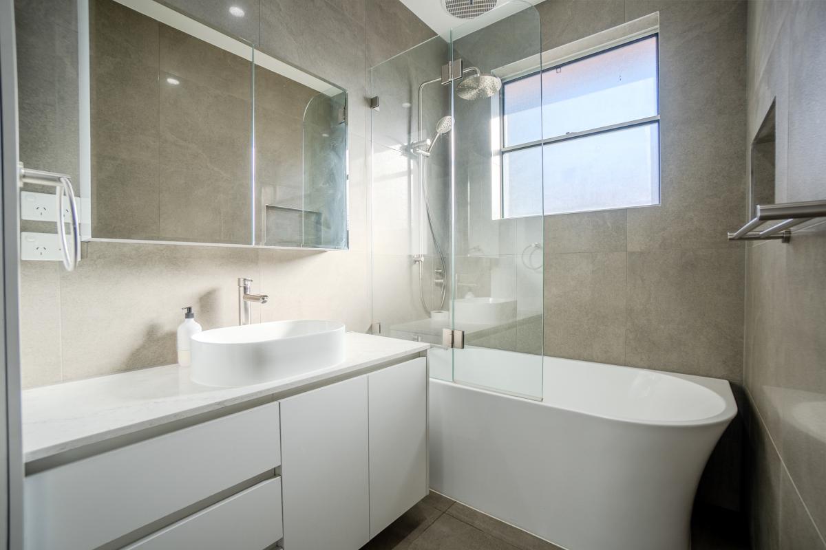 Modern luxury bathroom with white freestanding bath, glass shower screen, and grey stone tiles