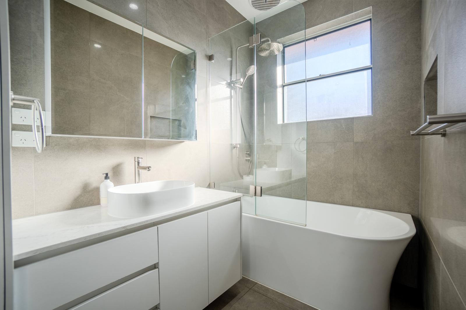Modern luxury bathroom with white freestanding bath, glass shower screen, and grey stone tiles